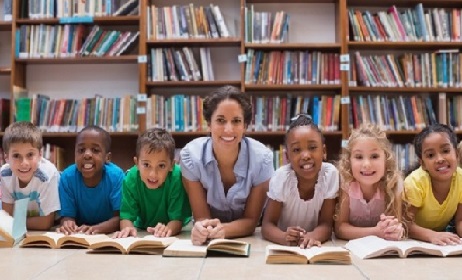 Cute pupils and teacher lying on floor in library