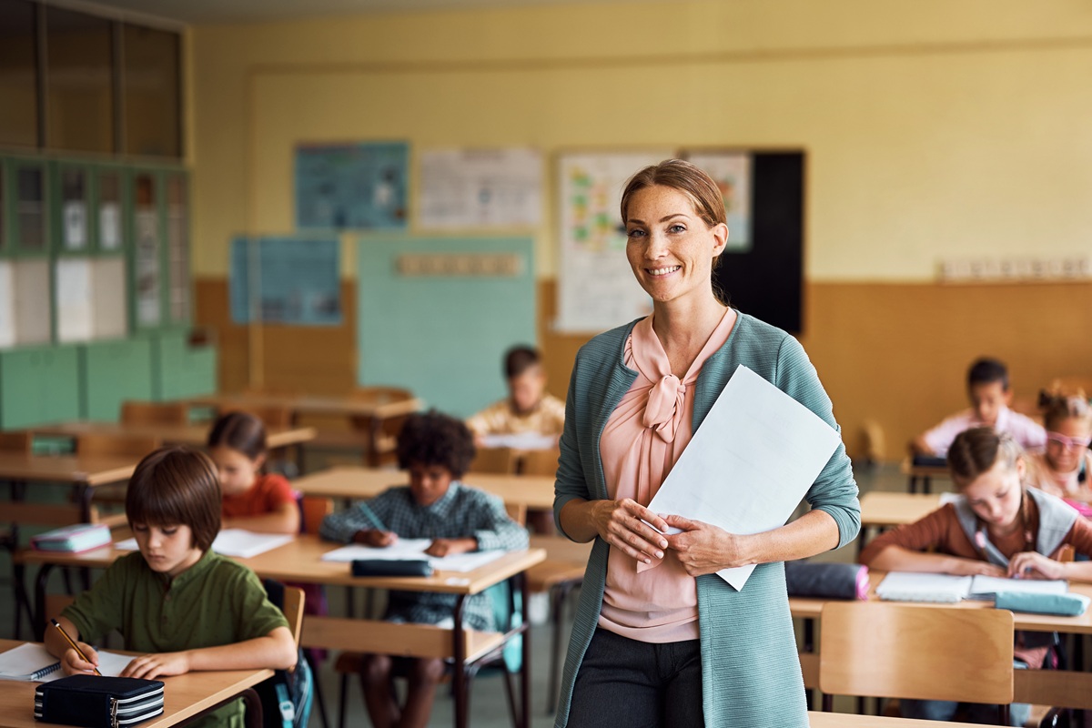 Happy elementary school teacher in classroom looking at camera.
