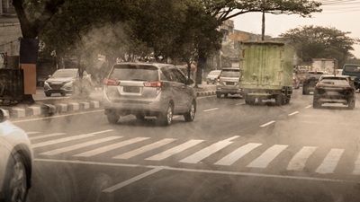 Busy urban traffic with cars and a truck driving through thick air pollution and smog on a city road. Represents environmental issues, climate change, and health risks in cities